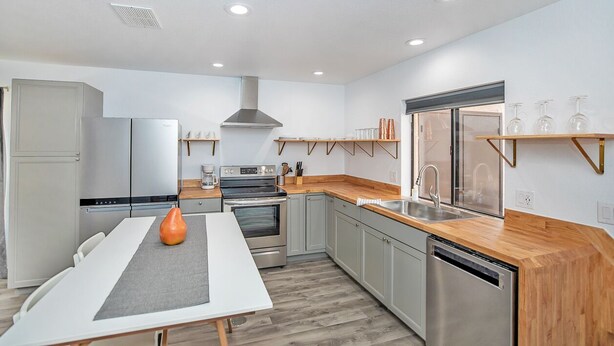 Una cocina moderna con electrodomésticos de acero inoxidable, una encimera de madera y un comedor con mesa blanca.