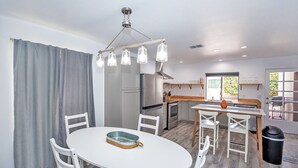 Una cocina moderna con comedor, muebles blancos y una lámpara colgante.