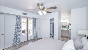 Un dormitorio con cama, ventilador de techo, vestidor y baño con lavamanos y espejo.