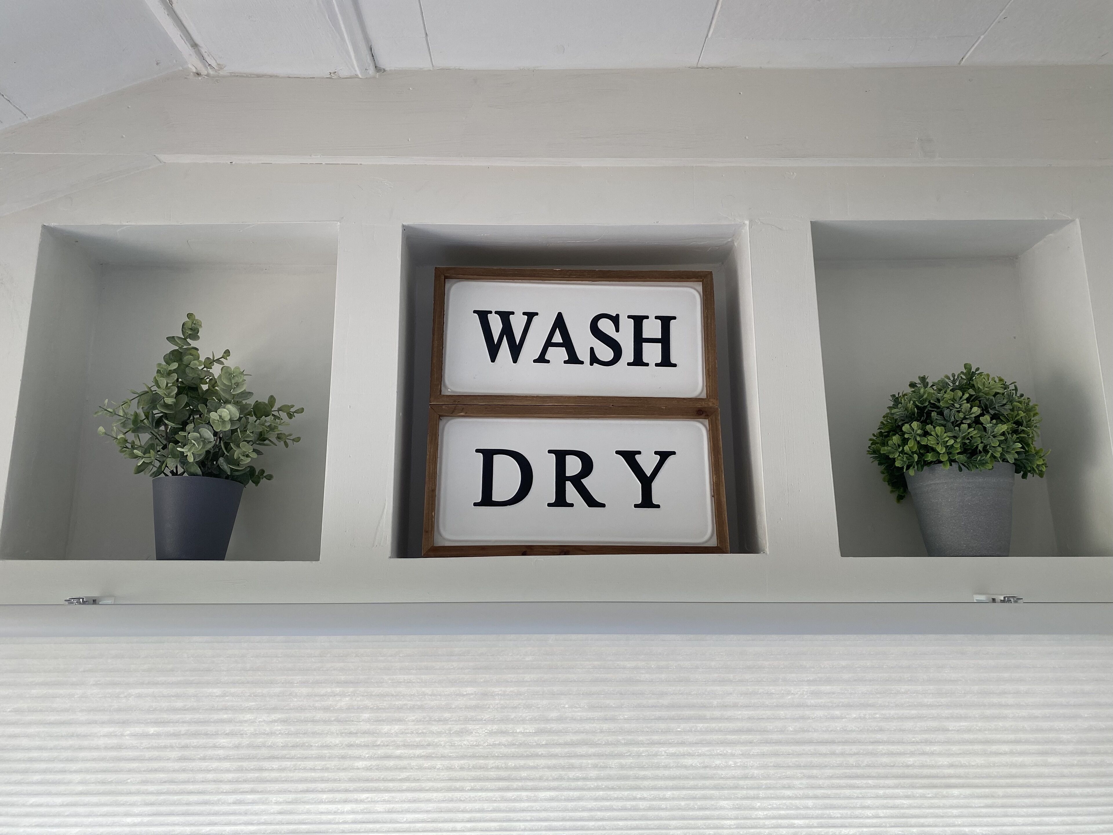 A wall-mounted shelf with two potted plants and a sign that reads "WASH DRY".