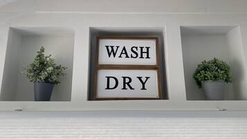 A wall-mounted shelf with two potted plants and a sign that reads "WASH DRY".