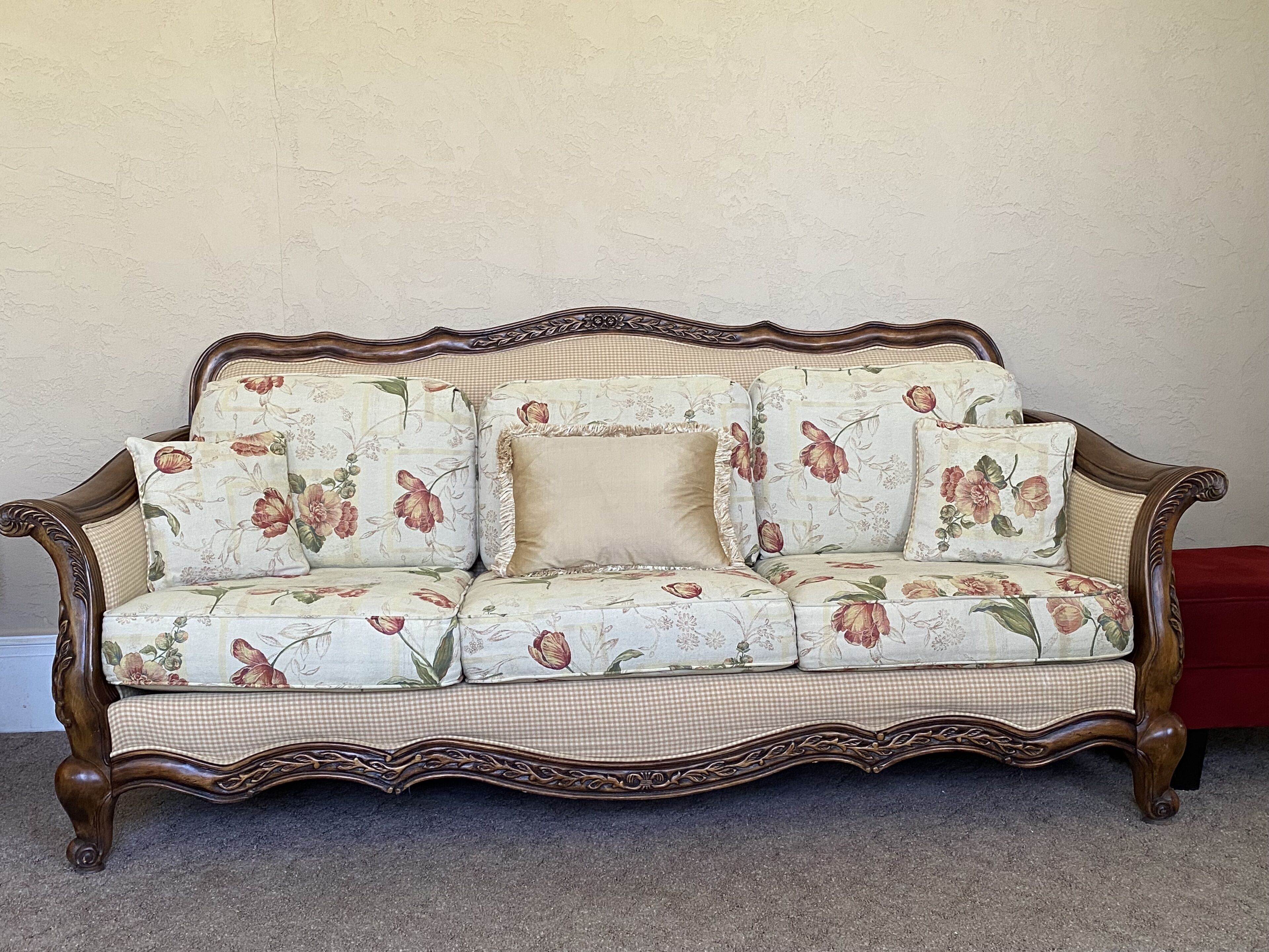 A vintage floral-patterned sofa with ornate wooden carvings, positioned against a plain wall.