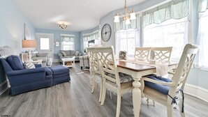 A spacious living room with a blue sofa, a dining table with white chairs, and a chandelier. - Beach Block Ocean Views Steps from the Boardwalk (Ocean City)