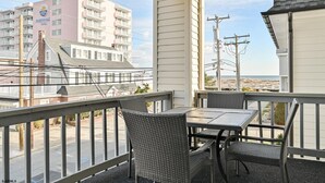A balcony with wicker chairs and a table, overlooking a beach and a hotel in the background. - Beach Block Ocean Views Steps from the Boardwalk (Ocean City)