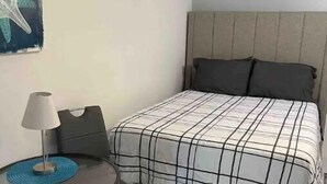 A bedroom with a bed, a bedside table with a lamp, a chair, and a starfish decoration on the wall. - Private suite, private entrance. (Deerfield Beach)