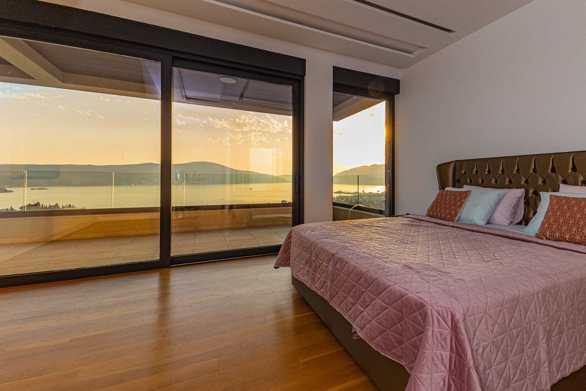 A bedroom with a large bed, a view of a body of water, and a balcony with glass doors.