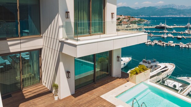 Ein modernes Gebäude mit Pool auf dem Dach, Außenbereich zum Sitzen und Blick auf einen Jachthafen.