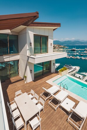 Un edificio moderno con piscina sul tetto, area salotto esterna e vista sul porto turistico.