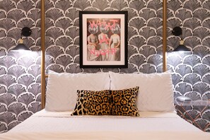 Une chambre avec un papier peint à motifs, un tableau encadré au mur, un lit avec un oreiller blanc à imprimé léopard et deux lampes de chevet.