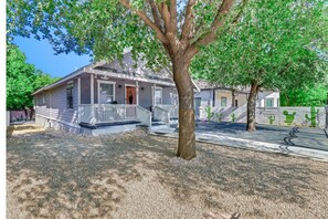 Une maison de plain-pied avec un porche, une allée et un arbre devant.