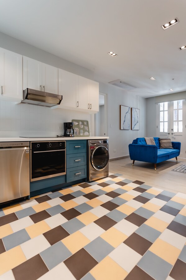 A modern kitchen with stainless steel appliances, a blue sofa, and a patterned floor.