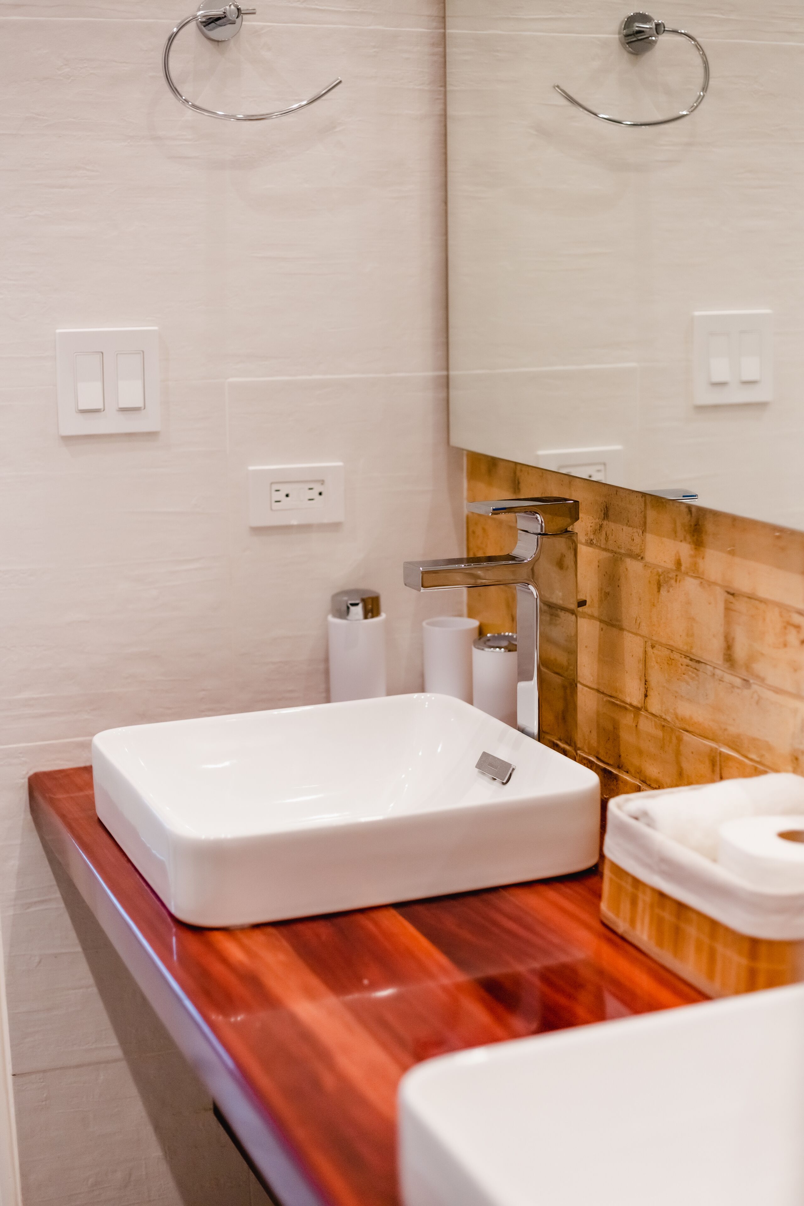 A bathroom with a white sink, a wooden countertop, a mirror, and a towel dispenser.