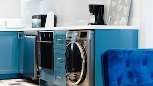 Una cocina moderna con armarios azules, lavavajillas, lavadora y cafetera.