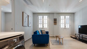 Una sala de estar moderna con un sofá azul, un televisor de pantalla plana y una lavadora en una esquina.