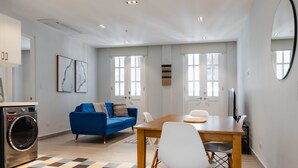 Una sala moderna con piso a cuadros, un sofá azul, una mesa de comedor de madera y una lavadora.
