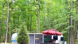 A mobile home with a red awning, surrounded by a forest. - Luxury, modern AIRSTREAM at June Farms! (West Sand Lake)