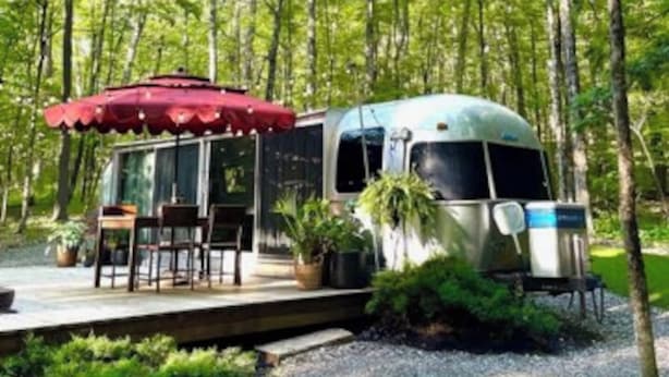 A mobile home with a covered patio area, surrounded by trees. - Luxury, modern AIRSTREAM at June Farms! (West Sand Lake)