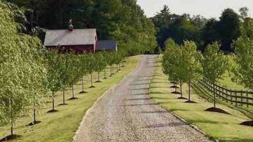 A gravel path leading to a red building with a sloped roof, surrounded by young trees and a wooden fence.