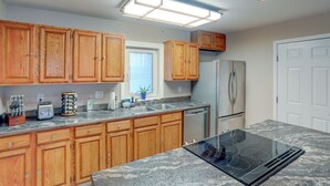 Una cocina con armarios de madera, un refrigerador de acero inoxidable, horno empotrado y encimera de granito.