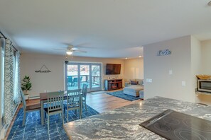 A modern kitchen with a built-in stove, a dining area with chairs and a table, and a living room with a sofa and a TV.