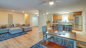 Una sala de estar moderna con un sofá modular, una mesa de comedor con sillas y una cocina con armarios de madera y un refrigerador.