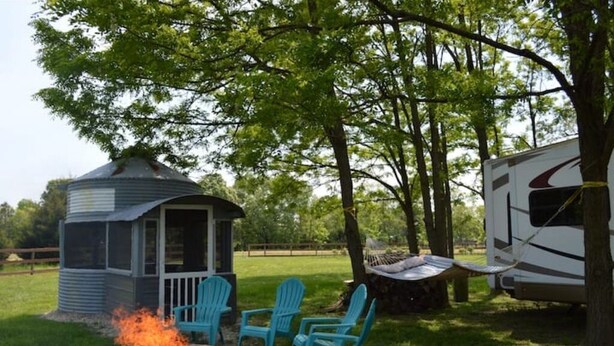 A gazebo with a fire pit and blue Adirondack chairs in a grassy area with trees and a white RV. - Waterfront at the Pines of Canoe Neck (Abell)