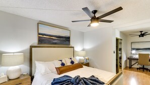 A bedroom with a bed, nightstands, a desk, and a ceiling fan.