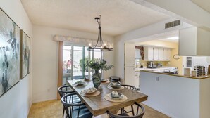 A dining area with a wooden table, chairs, and a chandelier. There is a vase with flowers on the table.