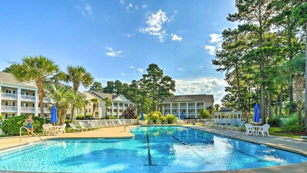 A swimming pool with lounge chairs and umbrellas, surrounded by buildings and trees. - Myrtle Beach Condo w/ Pool: Near Golf & Mall! (Myrtle Beach)