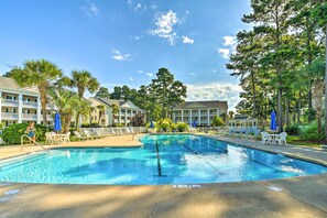 A swimming pool with lounge chairs and umbrellas, surrounded by buildings and trees. - Myrtle Beach Condo w/ Pool: Near Golf & Mall! (Myrtle Beach)