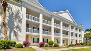A multi-story hotel with a symmetrical facade, balconies, and a well-maintained garden with various shrubs and flowers. - Myrtle Beach Condo w/ Pool: Near Golf & Mall! (Myrtle Beach)