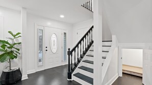 Um interior claro e branco com soalho de madeira escura, uma escadaria preta e um vaso de planta.