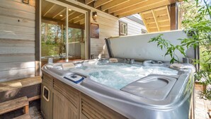 An outdoor hot tub area with wooden deck and glass doors leading to a covered patio.