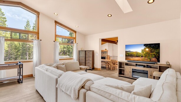 A spacious living room with a large sectional sofa, a flat-screen TV, and a dining area with a wooden table and chairs.