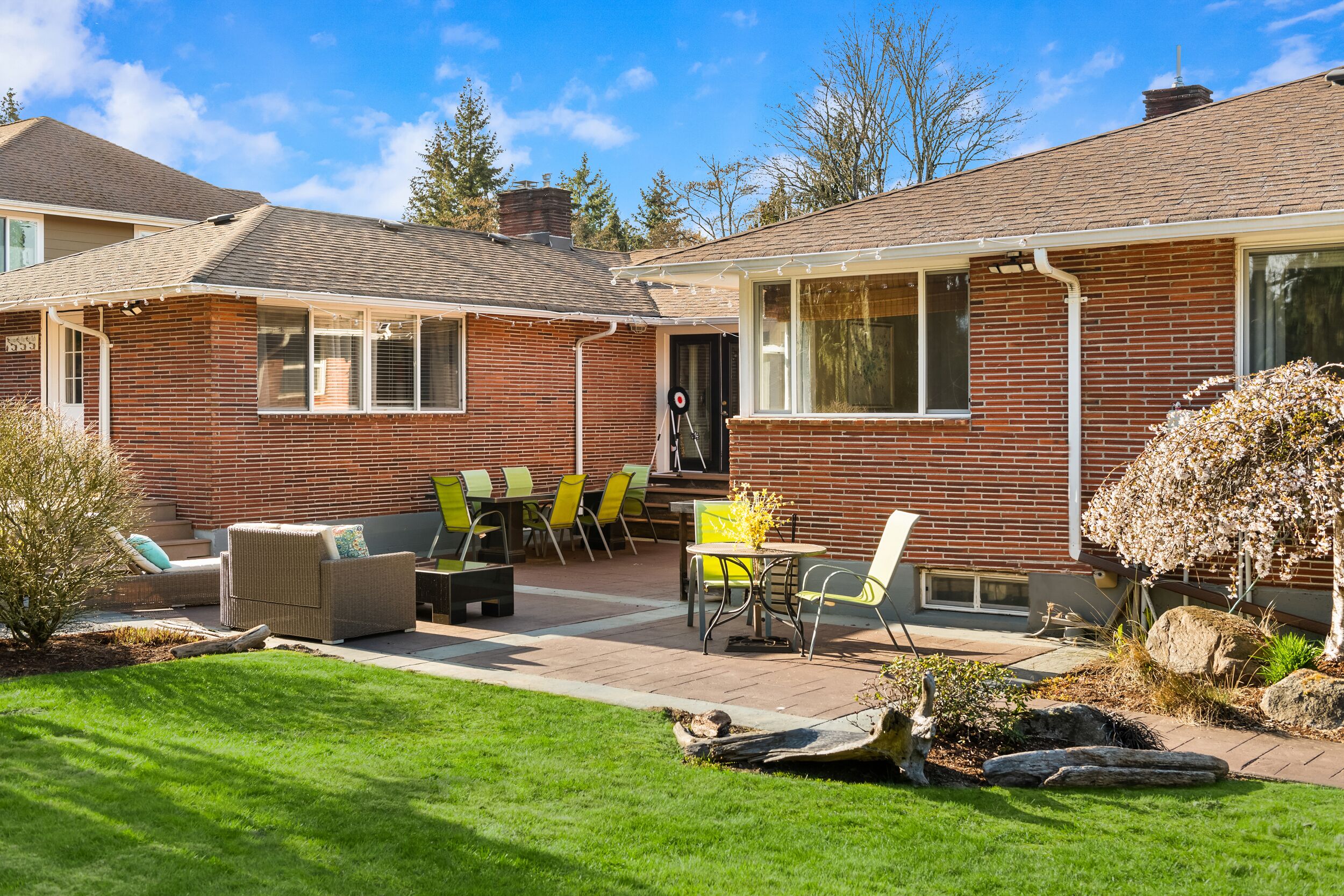 Une maison d’habitation dotée d’un patio aménagé avec des meubles d’extérieur, une façade en briques et une pelouse bien entretenue.