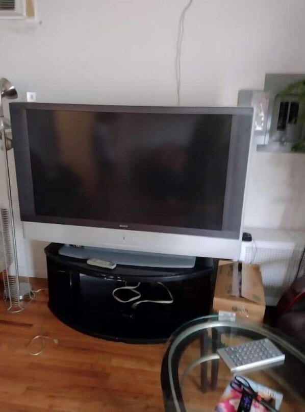A flat-screen TV on a stand, a glass table with a keyboard, and a white wall.