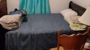 A small, simple room with a bed, a chair, and a desk.