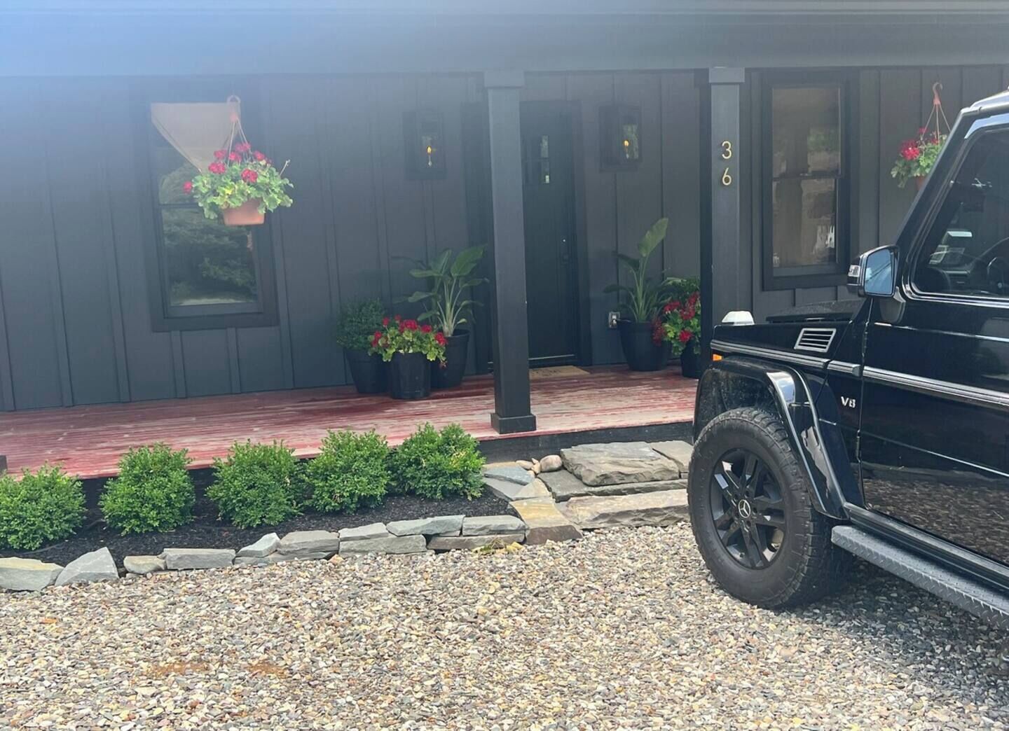 A black SUV parked in front of a house with a gravel driveway, a stone border, and potted plants.