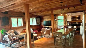 Interior espacioso de una cabaña con piso de madera, un sofá, sillas, una mesa de comedor y una cocina con electrodomésticos modernos.