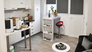 Una cocina compacta con armarios blancos, un comedor con mesa redonda y un sofá negro.