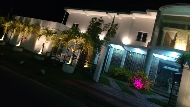 A modern building with a white facade, a gated entrance, and a well-maintained garden with palm trees and flowering plants. - Randima Hotels (Negombo)