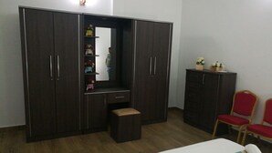 A bedroom with a bed, a wardrobe, a small stool, and two red chairs. - Randima Hotels (Negombo)