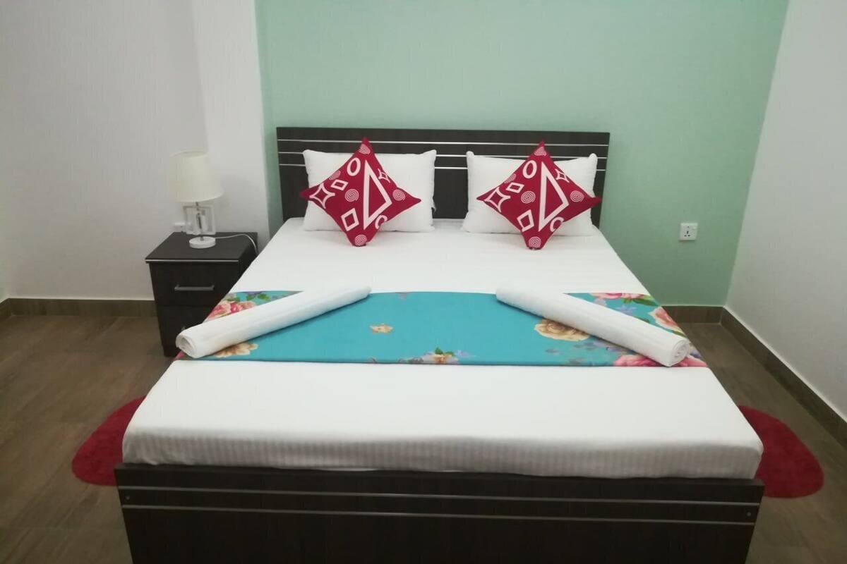 Cama bem arrumada com colcha floral, duas almofadas decorativas e uma toalha branca enrolada.