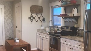A modern kitchen with white cabinets, a stainless steel refrigerator, and a dining area with a wooden table and chairs. - House in Forney (Forney)