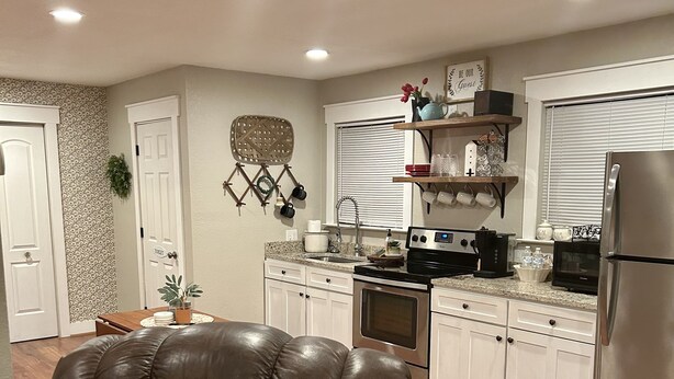 A modern kitchen with white cabinets, stainless steel appliances, and a brown leather sofa with cushions. - House in Forney (Forney)