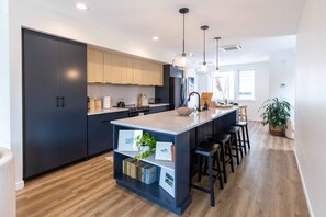 A modern kitchen with dark cabinets, a central island with bar stools, pendant lighting, and a wooden floor. - New Downtown Hailey Condo with Rooftop Hot Tub (Hailey)