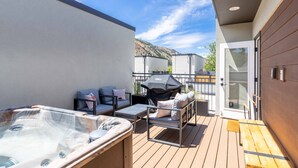 A deck with a hot tub, outdoor seating, and a grill.