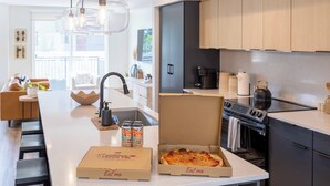 A modern kitchen with a central island, a stove, and a sink. There are two pizza boxes and two cans of beer on the island.