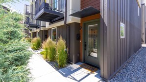 A modern apartment building with balconies, a wooden door, and a welcome mat.