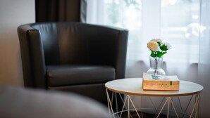 A modern room with a leather armchair, a round table with a book and a vase of flowers, and a view of the outdoors through large windows. - Mola Apartments-Wetter/ 5 P/Parking/Terrasse/Grill (Wetter (Ruhr))